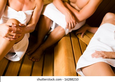 Three people, one male, two female, enjoying a hot sauna (no faces, focus on hand of man)