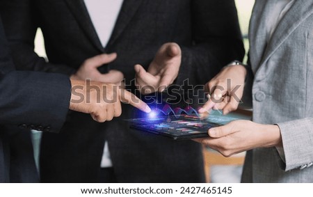 Three people are pointing at a tablet with graphs and market data.