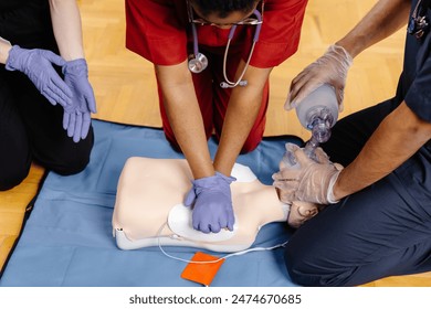 Three people are practicing CPR on a training mannequin. One person is performing chest compressions while another is using a bag valve mask to give breaths.