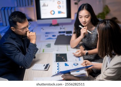 Three people are sitting at a table with papers and graphs in front of them. They are discussing something important, possibly related to business or finance. The atmosphere seems serious and focused - Powered by Shutterstock