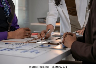 Three people are sitting at a table with papers and a pen. They are discussing something important. Scene is serious and focused