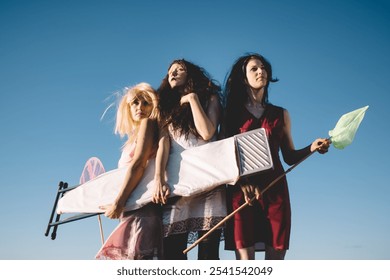 Three people stand on a large beach rock, facing the ocean with a sail and net. The vibrant scene highlights friendship, adventure, and a carefree moment under a vast, clear sky - Powered by Shutterstock