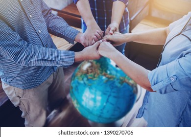 Three people standing and holding hands each other while pray to God for the world over blurred world globe on wooden table, Christian background for great commission or earth day concept.