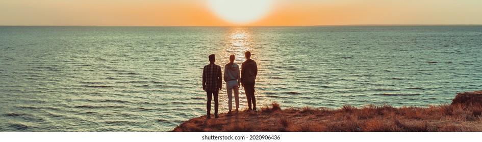 The three people standing on the mountain peak near the sea