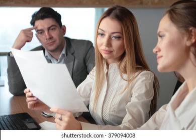 Three People Studying The Paper In The Office At The Table