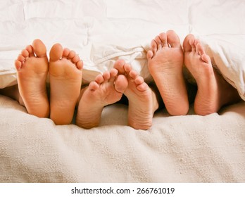 Three People Under The Covers With Feet Showing In A Bed