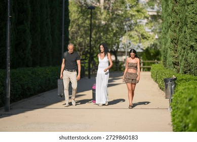 Three people walking down a path, one of them carrying a skateboard. The woman in the white dress is carrying a suitcase