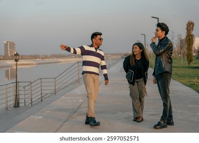 Three people are walking down a sidewalk near a body of water. One of them is pointing to something in the distance