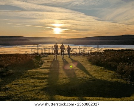 Three people walking into cloud inversion at sunset, Sugar Loaf, Abergavenny, Wales, UK