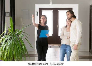 Three Person Standing In Hallway. Smiling Real Estate Agent, Realtor Showing Property House For Sale Or Tenant To Young Happy Married Couple. New Home, Moving And Realestate Loan And Mortgage Concept