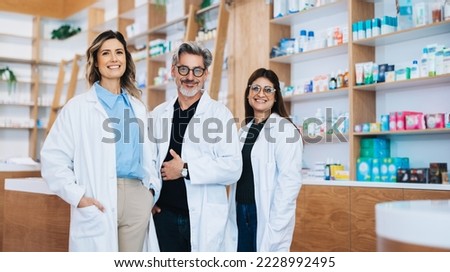 Three pharmacists standing together and looking at the camera in a drug store. Group of healthcare professionals working in a pharmacy.