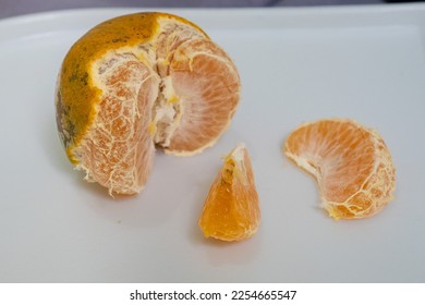 three pieces of orange, one that still has peel, one orange that has been bitten or cut, one more orange that is ready to eat on a white cutting board - Shutterstock ID 2254665547