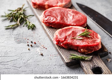 Three pieces of traditional thin steak cut from the tenderloin on wooden cutting board with olive oil, salt, rosemary and pepper. Raw Black Angus Prime meat steaks suitable for grilling or frying pan. - Powered by Shutterstock