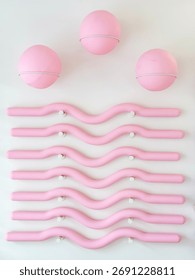 Three pink Pilates balls and several wavy rods are mounted on a white wall in a gym or fitness center. Aesthetic focus on balance and physical activity.