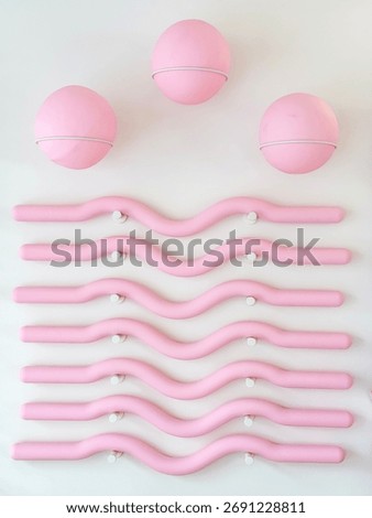Three pink Pilates balls and several wavy rods are mounted on a white wall in a gym or fitness center. Aesthetic focus on balance and physical activity.