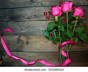 Three Pink Roses Lie On A Wooden Surface, Tied With A Pink Ribbon Run Along The Edge. Postcard With A Declaration Of Love, Valentine's Day.