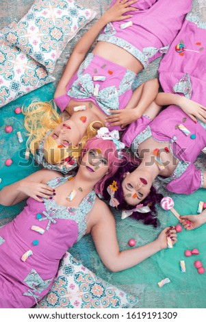 Three pinup girls with purple dresses on the ground posing with candy.
