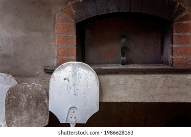 Three pizza paddles standing in front of a brick pizza oven