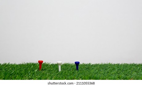 Three Plastic Golf Tees, Showing A Red White And Blue Standard Ball Pin On Artificial Green Grass.