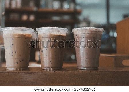 Three plastic take away cups of iced coffee mocha, iced coffee latte and iced chocolate on table with blurred background