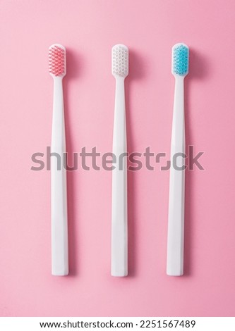 Three plastic toothbrushes on a pink background in pastel colors. Flat lay, top view.
