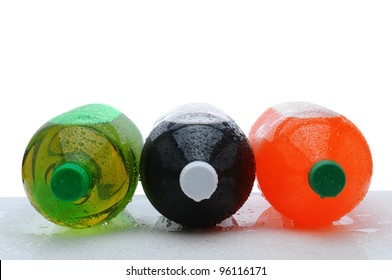 Three plastic two liter soda bottles laying on their sides with condensation on a wet counter. Horizontal format over a white background.