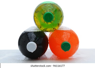 Three plastic two liter soda bottles laying on their sides stacked in pyramid shape with condensation on a wet counter. Horizontal format over a white background.