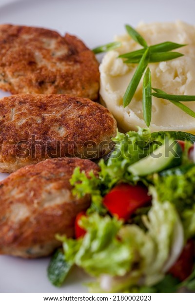 Three pork cutlets\
with mashed potatoes and cucumber, tomato and lettuce salad. The\
food is on a white plate.