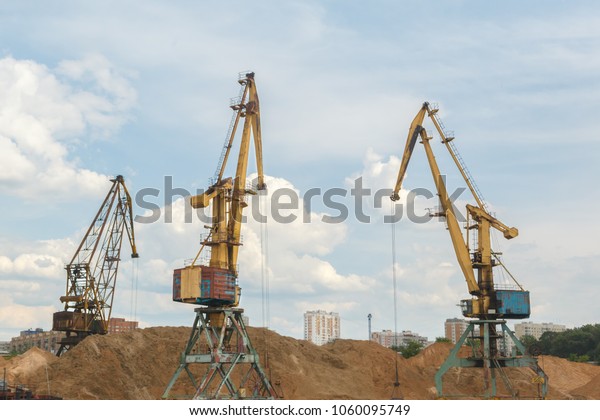 Three port crane\
loading sand. Urban\
landscape