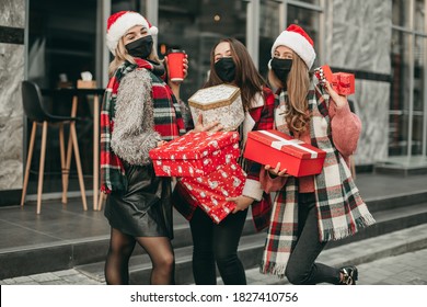 Three portrait of young happy women in red Christmas clothes, medical masks, hats and gifts walking in the city and shopping in quarantine. New year, boxes, girlfriends, shop, coronavirus, pandemic