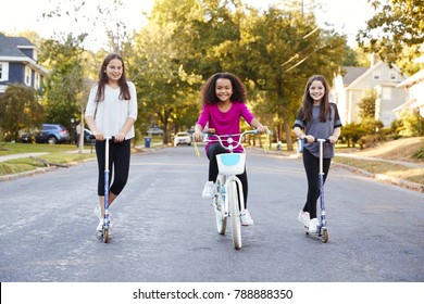 Three pre-teen girls on scooters and bike looking to camera