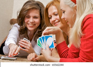 Three pretty girls lying on the floor, playing a game of cards UNO.