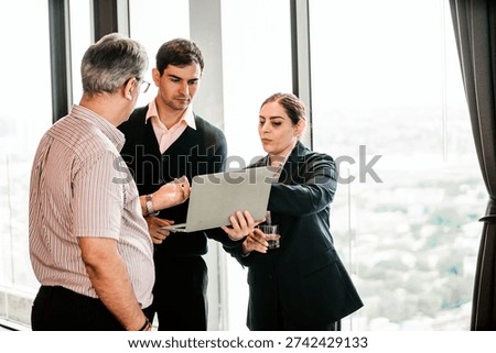Three professionals discuss data on a laptop during a meeting in a high-rise office with city views.