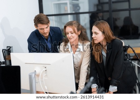 Three professionals engage in a collaborative discussion in a contemporary office. They focus on analyzing data displayed on a computer monitor, fostering teamwork and communication.