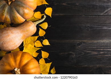 Three pumpkins of different sizes on a black wooden background with yellow leaves. Located on one side. Copy space. Top view.