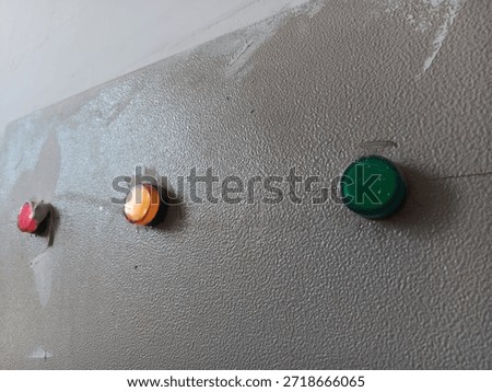 Three push button lamps on gray wall show red amber green light set with rough paint texture industrial control panel close view