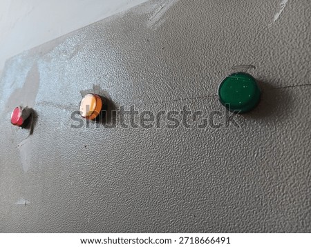 Three push button lamps on gray wall show red amber green light set with rough paint texture industrial control panel close view