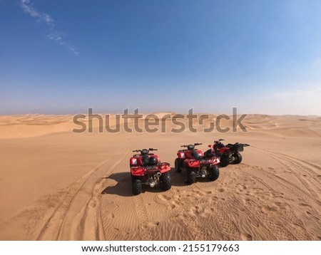 Three quad bikes parked in the middle of the desert near Swakopmund, Namibia, on a big dune with nothing else than a clear blue sky and more dunes in the distance. Vacation, adventure scene.  