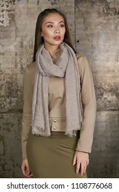 Three quarter isolated studio portrait of a young Asian lady in an olive skirt, a beige jacket and a grey scarf. The brunette girl posing over the grunge rusty background, looking to the side.