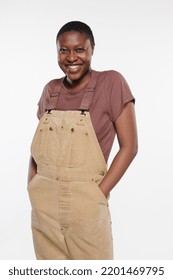 Three quarter length portrait of a Non-binary Afro-Latino in their 20s smiling with hands in pockets on a neutral background