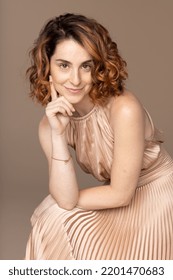 three quarter length shot of beautiful caucasian woman in her 20s confidently wearing a gorgeous dress and sitting on a stool on neutral background Stock Photo