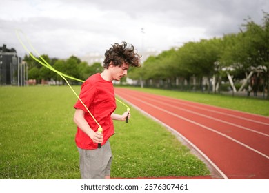 Three quarter length side view photo of a caucasian young man exercising skipping rope in a running track outdoors