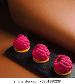 Three raspberry mousse desserts arranged on a black slate, showcasing modern confectionery