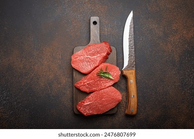 Three raw uncooked meat beef top sirloin steaks on wooden cutting board with rosemary on wooden cutting board with knife on dark rustic background top view, preparing meal with meat - Powered by Shutterstock