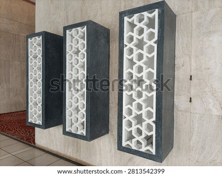 Three rectangular black stone boxes with openwork white geometric star screens mounted vertically on a beige textured marble wall.