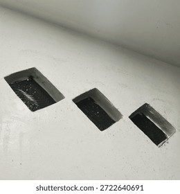 Three rectangular openings in a white wall appear to be filled with a dark, possibly wet, sealant or paint.