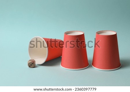 Three red cups and dice on light blue background. Thimblerig game