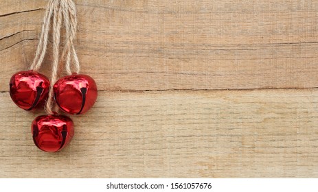 Three Red Jingle Bells Hanging On Rope Against A Wood Background With Writing Space