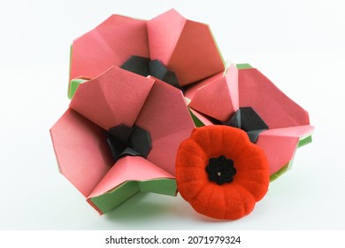 Three red origami poppies on a white background with black centers and green stems with a red velvet poppy in front of them