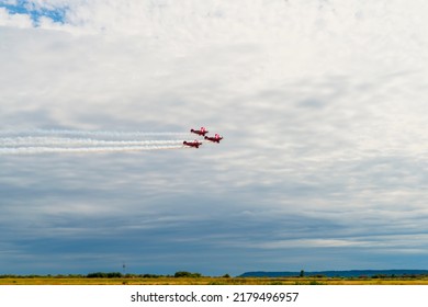 three red planes are flying in a cloudy sky over a yellow field